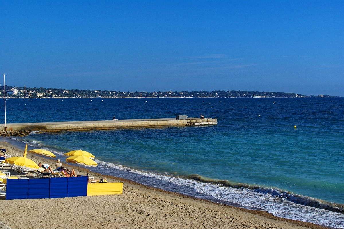 Plage de sable et parasols jaunes à Golfe-Juan avec vue sur le cap d'Antibes